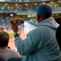 A man at a baseball game holding a hot dog, with a 'play' button over top