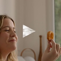 A woman holding an onion ring smiling, with a 'play' button over top