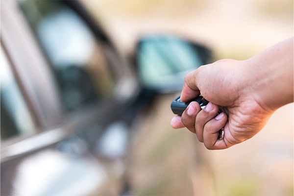 A person's hand holding and using a remote entry key to unlock a car.