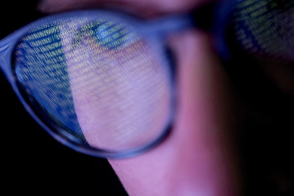 Close-up of a man wearing glasses with computer data reflecting in the lens.