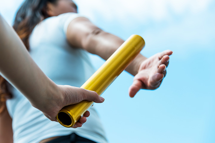 A hand passing a gold baton to a woman