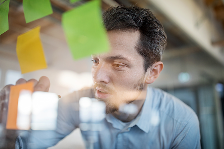 Young business man planning strategy with colourful Post-It Notes on a glass wall