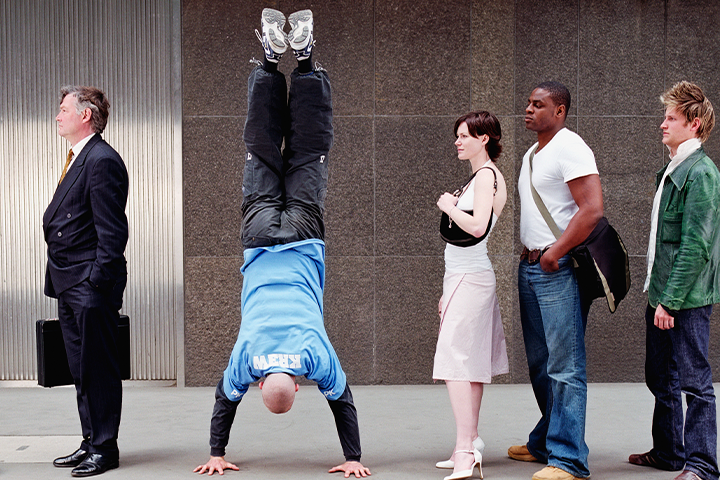 5 adults standing in line, with the second one of them doing a handstand.