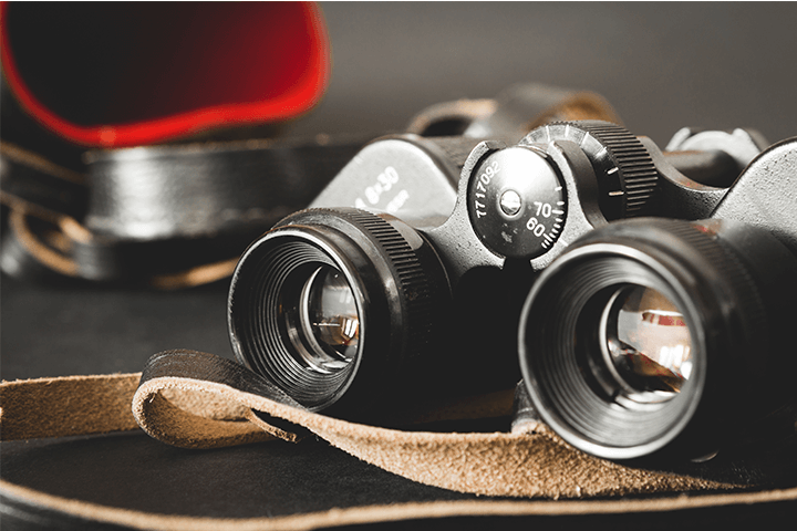 A pair of binoculars with a leather strap resting on a table.