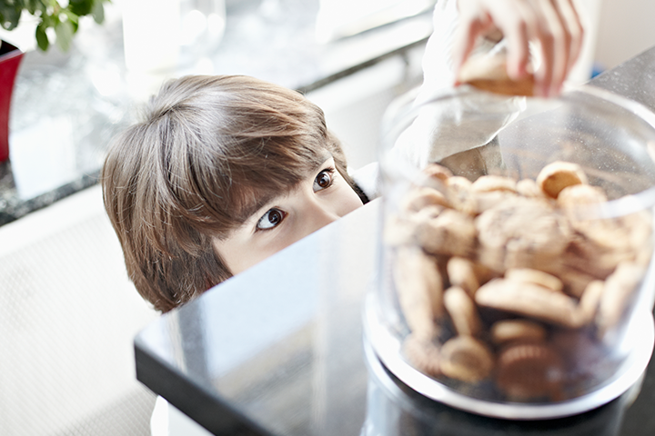 A young boy reaching for a cookie from a cookie jar