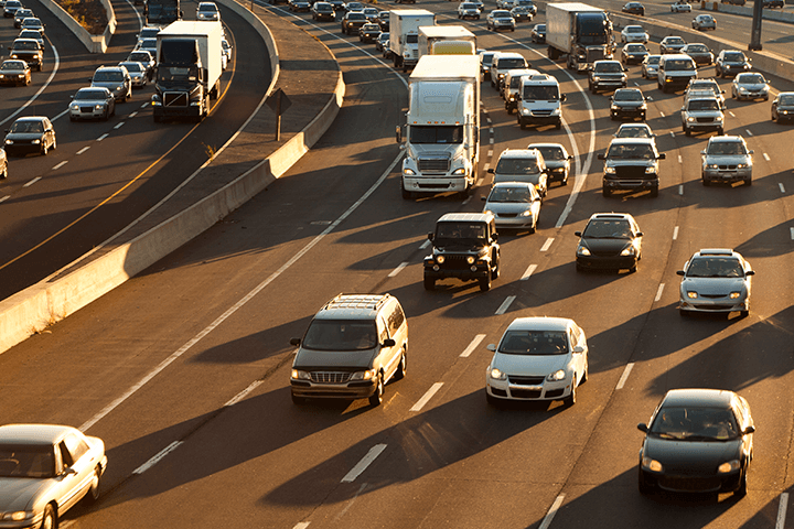 A busy highway at dawn, with many cars, vans and trucks driving around a curve.