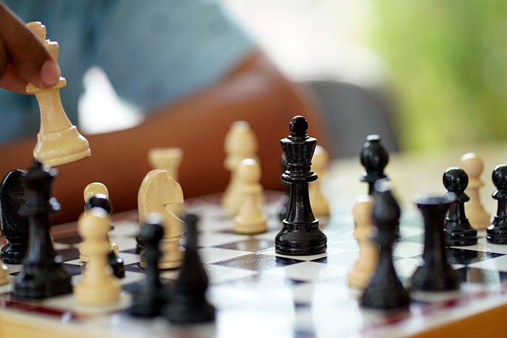 A chess board with a man moving his queen piece.