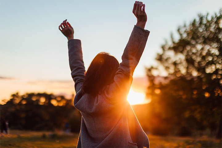 A woman raising her arms in a celebratory manner, looking at a sunset