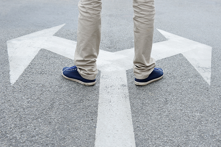 A man standing on pavement on top of an arrow splitting in two directions.