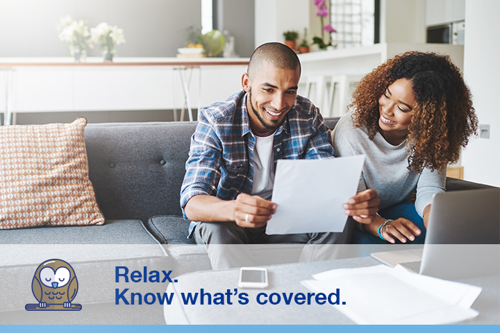 A couple sitting on their living room couch, looking at a piece of paper next to an open laptop computer. Image caption "Relax. Know what's covered" next to an illustration of an owl.