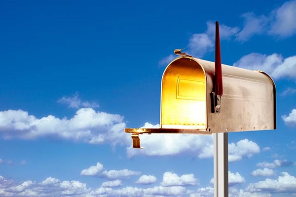 An open metal mailbox with a gold light shining from within, in front of a blue sky background.