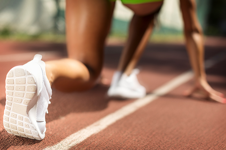 A woman kneeling down in start position before running a race on a track