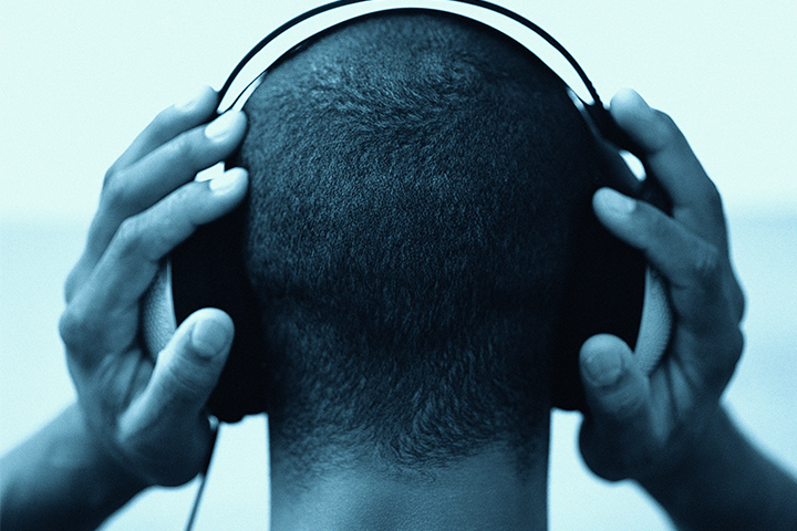 The back view of a man wearing headphones, with his hands clasping either side of the headphones.