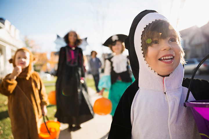 Group of small children trick or treating on Halloween, with a small boy dressed as a penguin in the forefront.