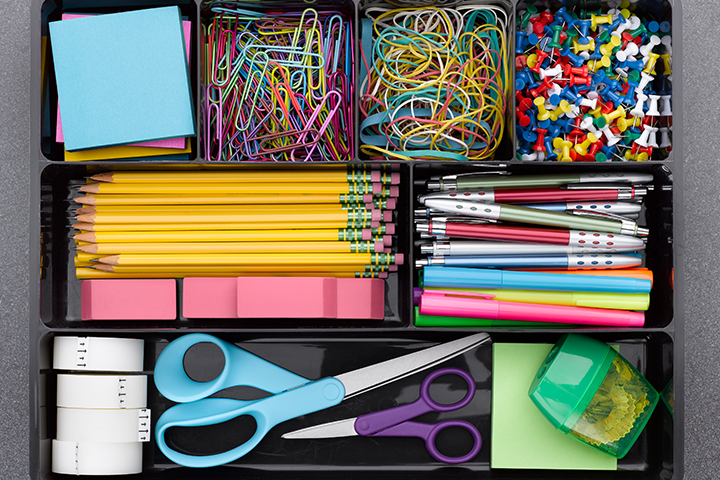 A tray full of colourful office supplies, including scissors, paperclips, pins and pencils, neatly organized in different compartments.