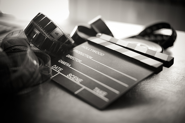 A black and white image of a movie clapperboard lying on a table with loose film strip.