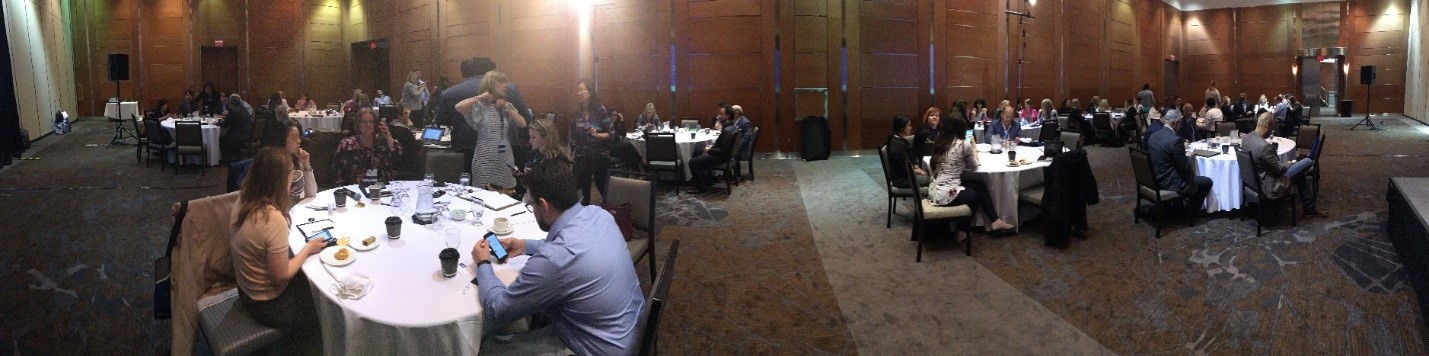 Panoramic shot of the Broker Forum event, with people sitting around ten large round tables talking.