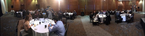 Panoramic shot of the Broker Forum event, with people sitting around ten large round tables talking.