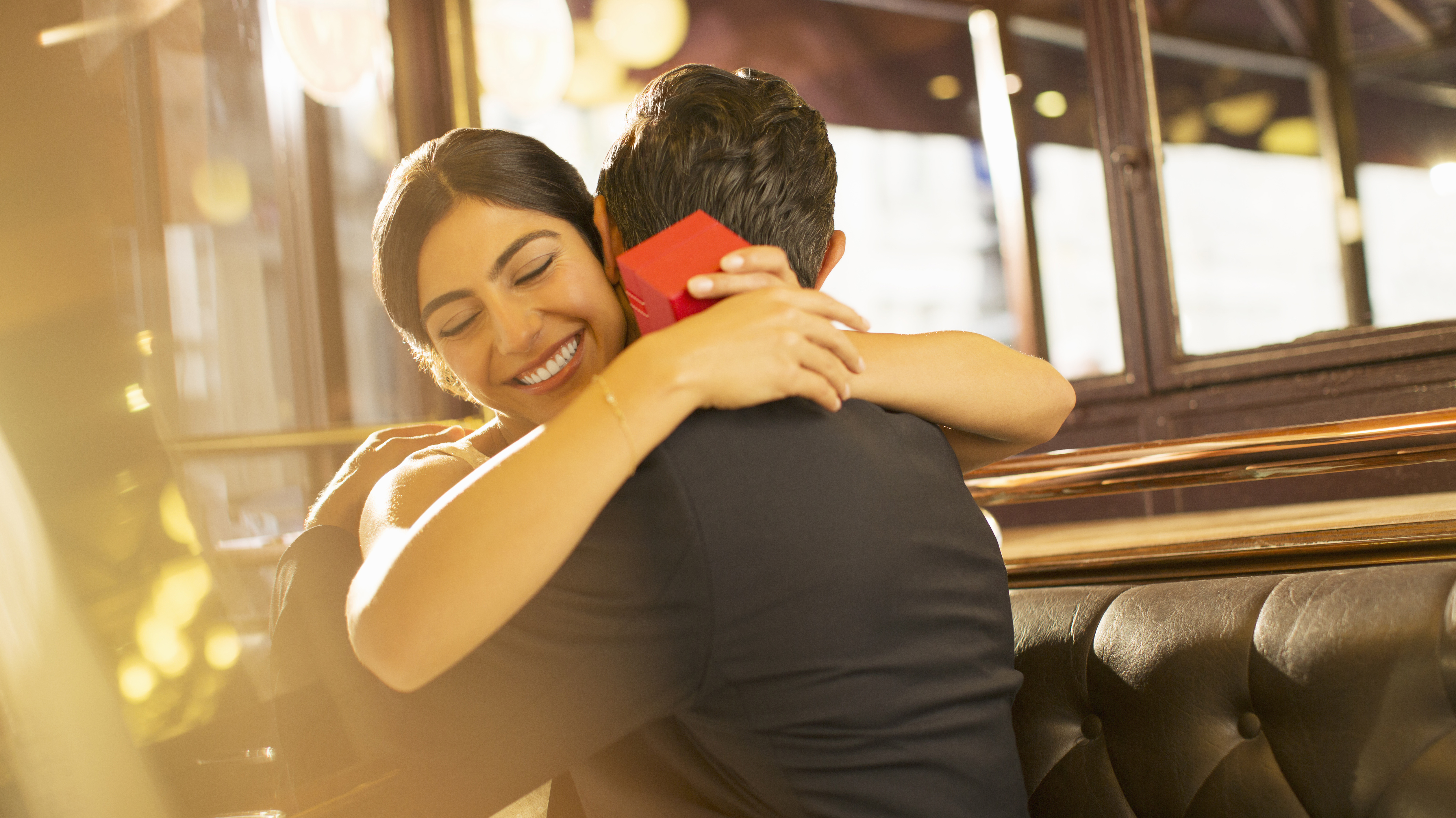 A Happy woman hugging her husband with a small red box (a gift) in her hands.