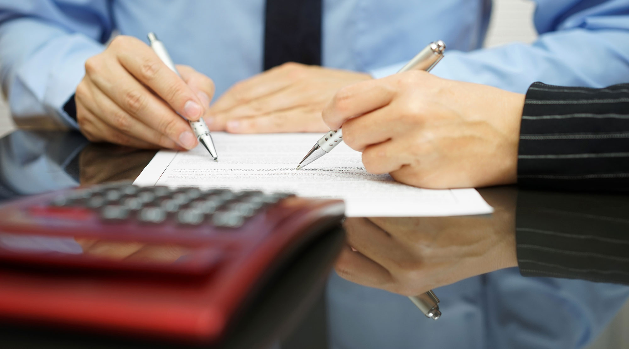 Male and female hands sitting at a desk pointing to a document holding pens.