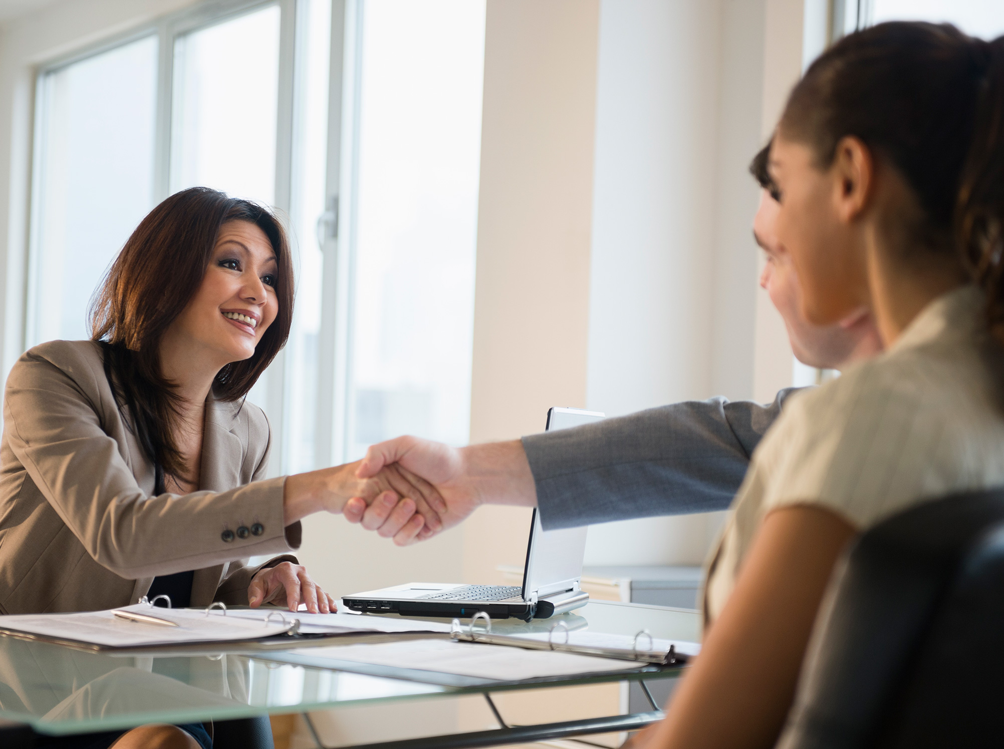 Insurance broker sitting across a desk from a young couple shaking a man's hand