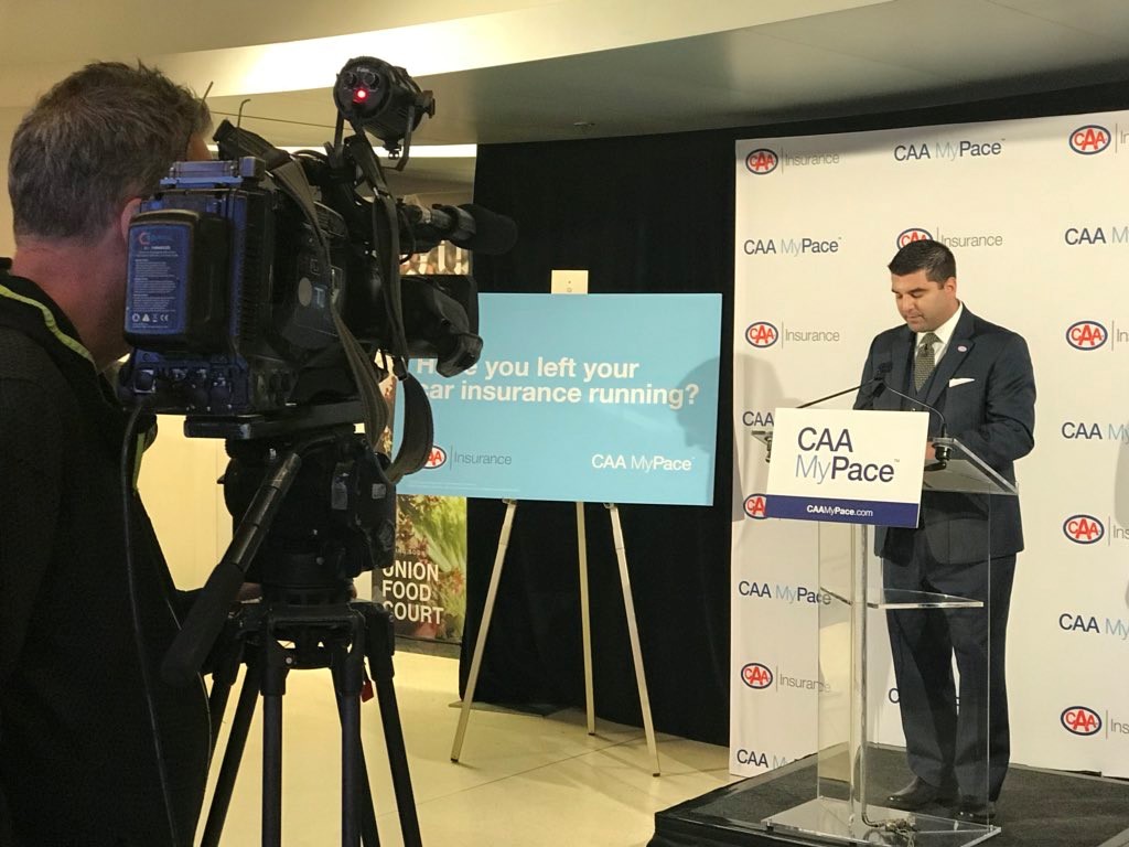 CAA Insurance President, Matthew Turack, standing at a podium making an announcement about CAA MyPace, while being filmed by a camera man.