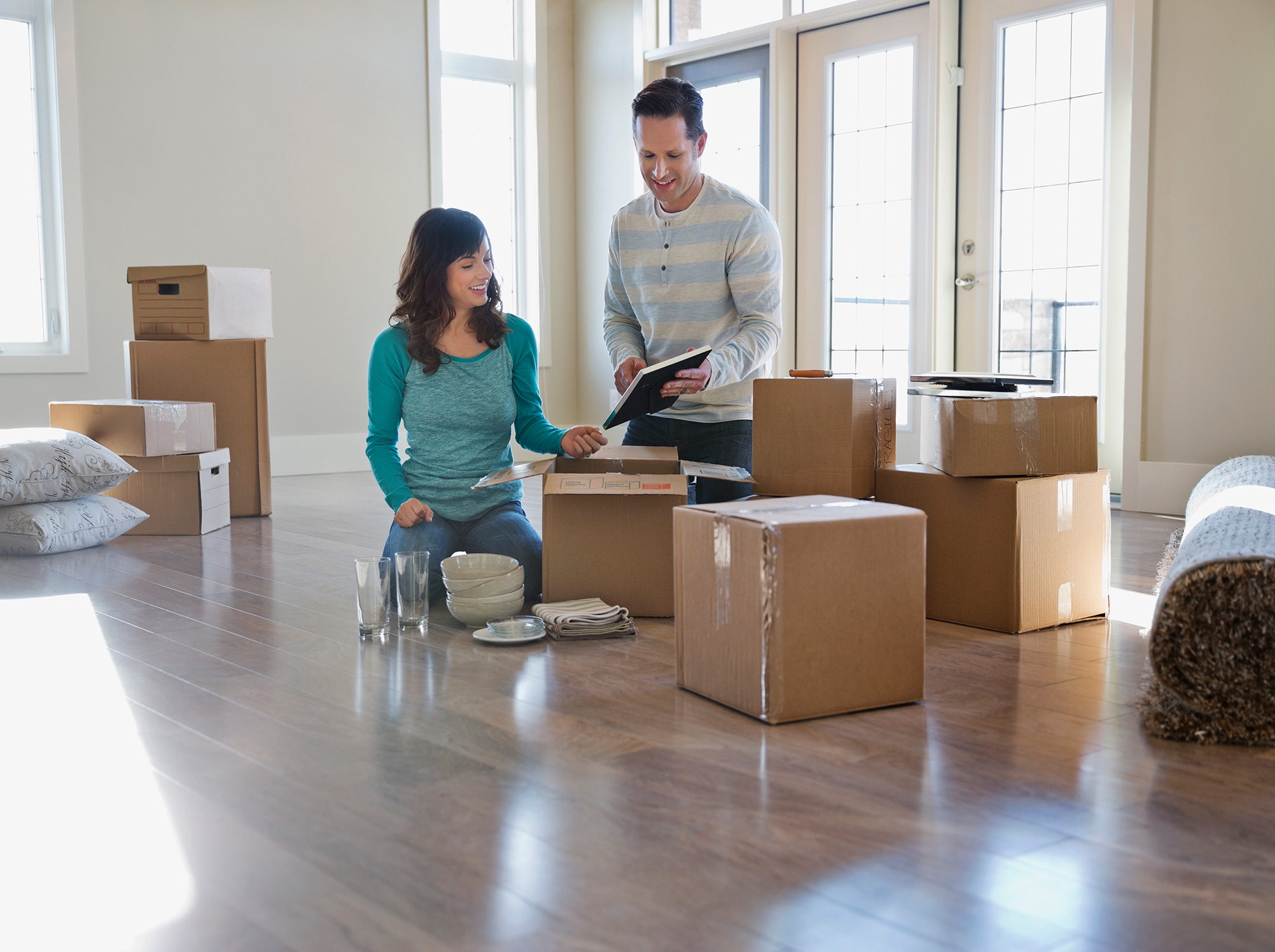 Young couple in an empty room with moving boxes holding a checklist